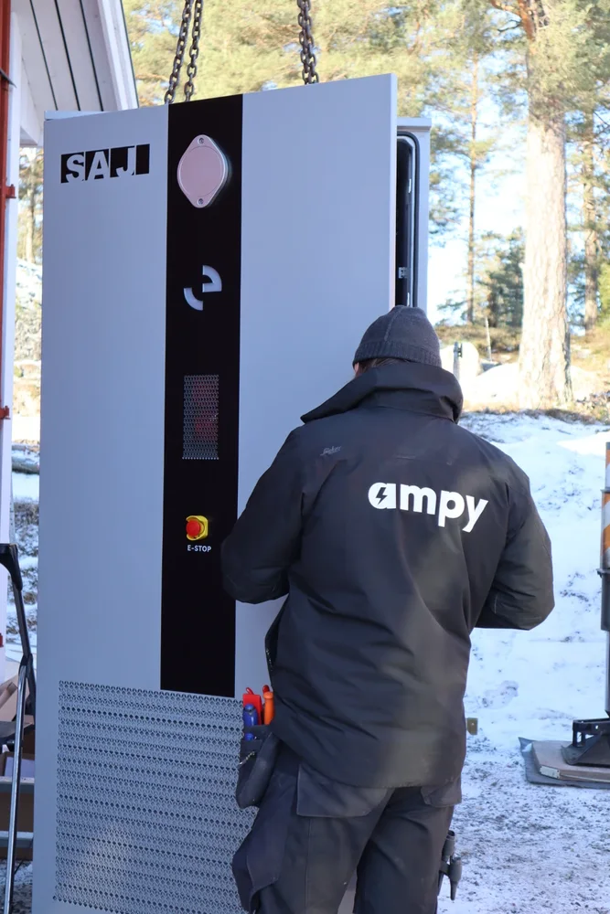 En elektriker med Ampy-jacka som övervakar installationen av ett komplett batterisystem.