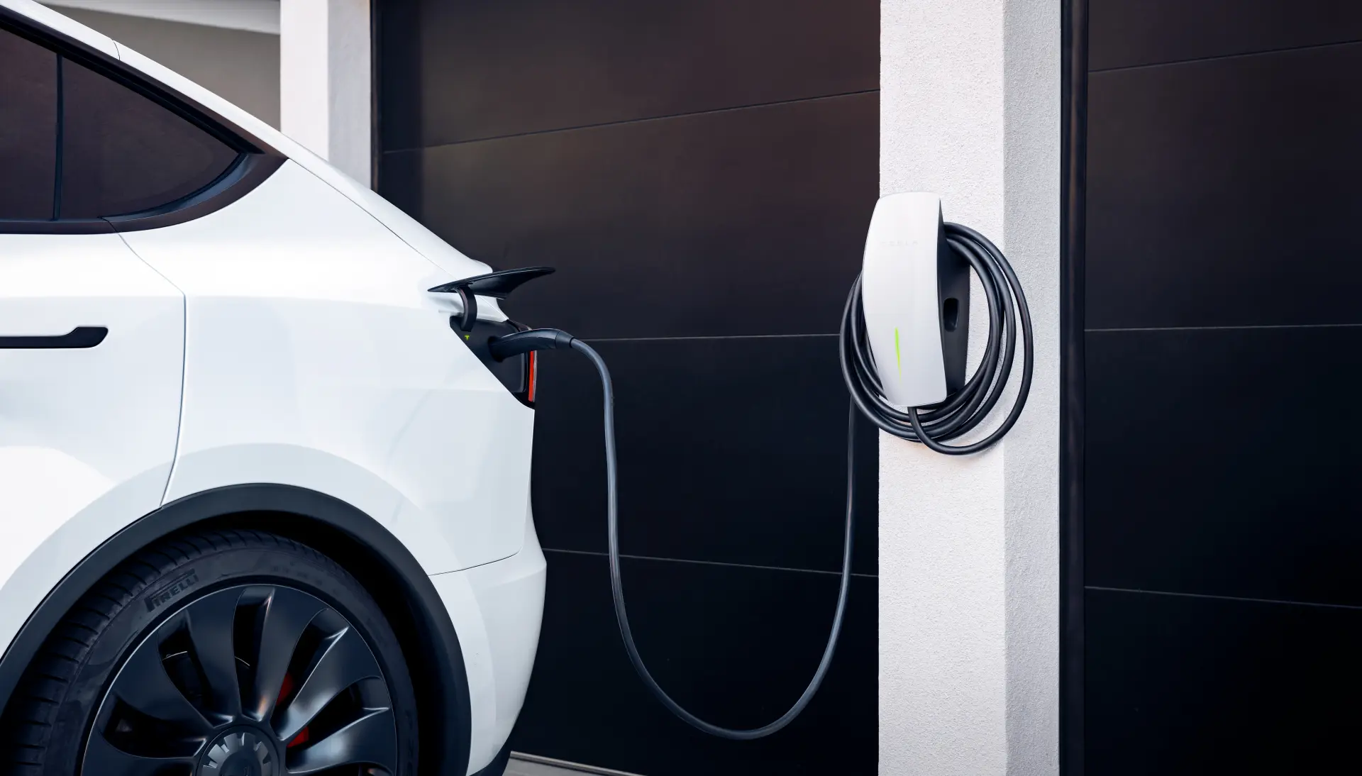 En elbil ansluten till en Tesla Wall Connector som signalerar aktiv laddning.