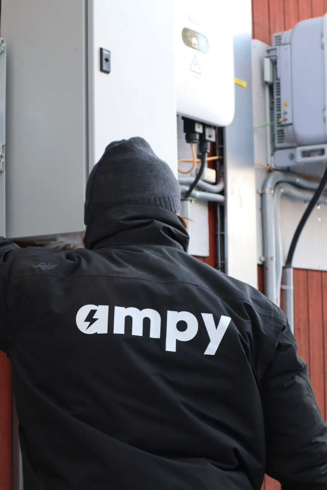 En elektriker med Ampy-logotyp på ryggen står framför ett nyinstallerat hemmabatteri.