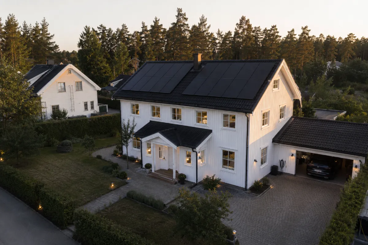 White house with solar panels, garden, and paved driveway.
